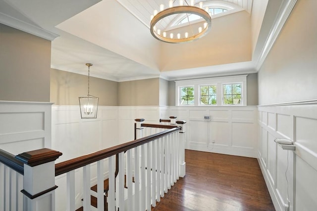 hallway with ornamental molding, dark wood finished floors, a decorative wall, and a notable chandelier