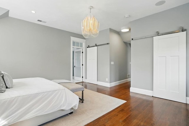 bedroom featuring an inviting chandelier, a barn door, baseboards, wood finished floors, and visible vents