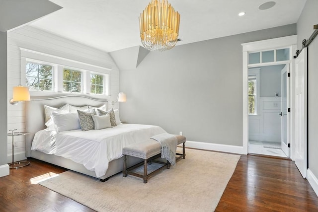 bedroom featuring wood finished floors, baseboards, a barn door, and a notable chandelier