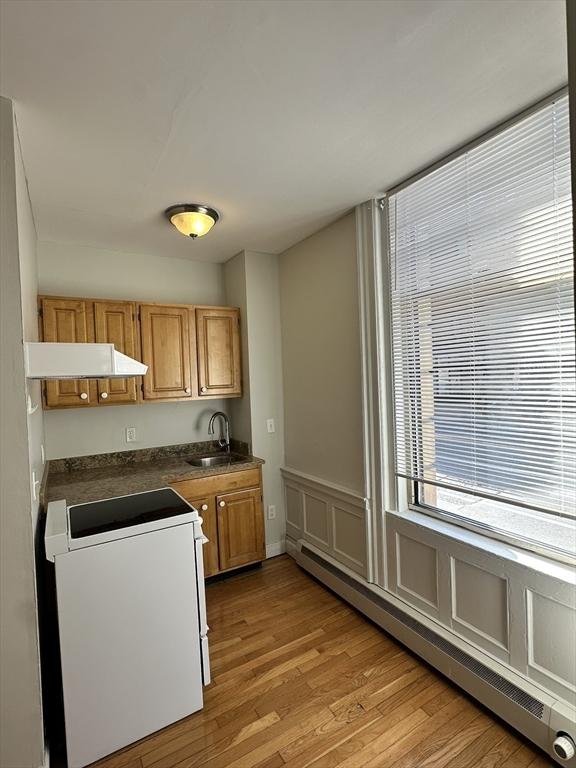 kitchen featuring stove, custom exhaust hood, a baseboard heating unit, sink, and light hardwood / wood-style flooring