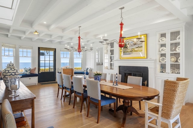 dining space with beam ceiling, light hardwood / wood-style flooring, a water view, and a chandelier