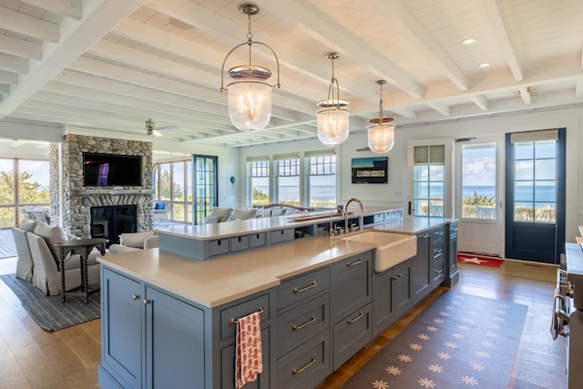 kitchen featuring a fireplace, an island with sink, beamed ceiling, dark hardwood / wood-style floors, and sink