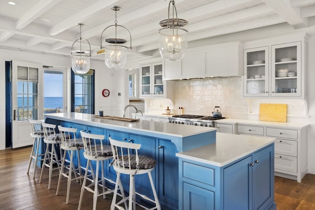 kitchen featuring a center island with sink, beam ceiling, dark wood-type flooring, backsplash, and blue cabinets