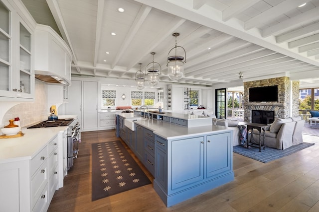 kitchen featuring a fireplace, pendant lighting, dark wood-type flooring, a large island with sink, and white cabinetry