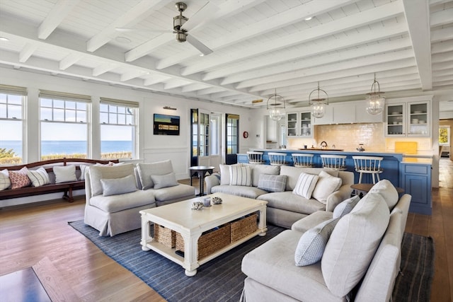 living room featuring beamed ceiling, a healthy amount of sunlight, dark hardwood / wood-style flooring, and a water view