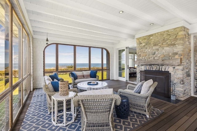 sunroom with beamed ceiling, a fireplace, and a water view