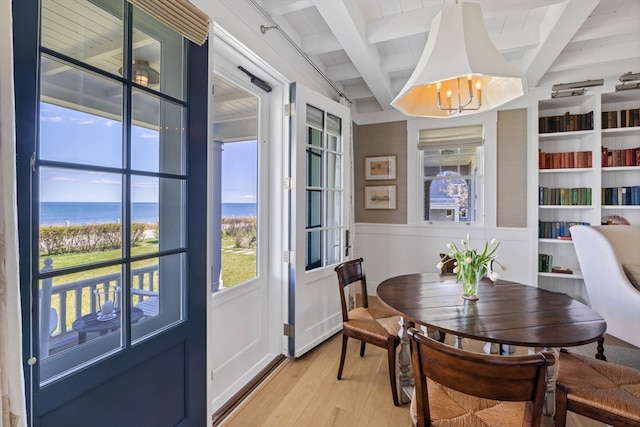 dining room with a notable chandelier, beam ceiling, a water view, and light hardwood / wood-style floors