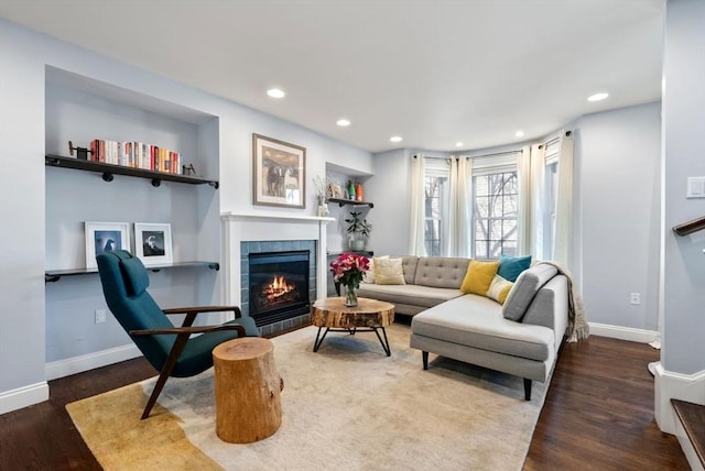 living area featuring a tiled fireplace, baseboards, wood finished floors, and recessed lighting