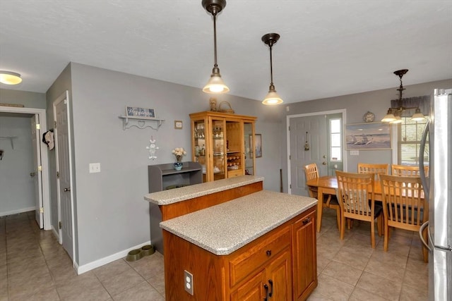kitchen featuring freestanding refrigerator, light countertops, a center island, decorative light fixtures, and light tile patterned floors