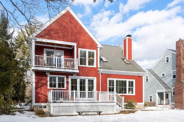 back of house featuring a balcony, a chimney, and roof with shingles