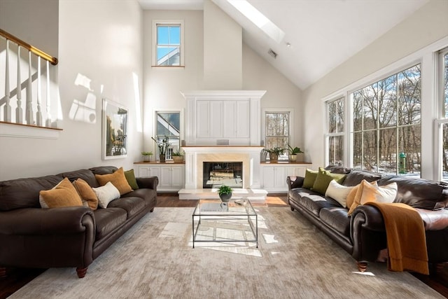 living room with a skylight, a fireplace, visible vents, wood finished floors, and high vaulted ceiling