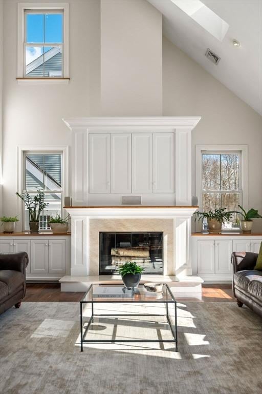 living area featuring a skylight, visible vents, a premium fireplace, wood finished floors, and high vaulted ceiling