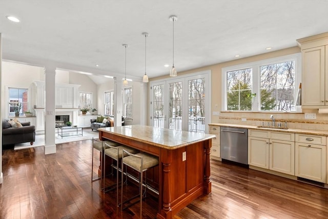 kitchen with a glass covered fireplace, open floor plan, cream cabinets, stainless steel dishwasher, and a sink