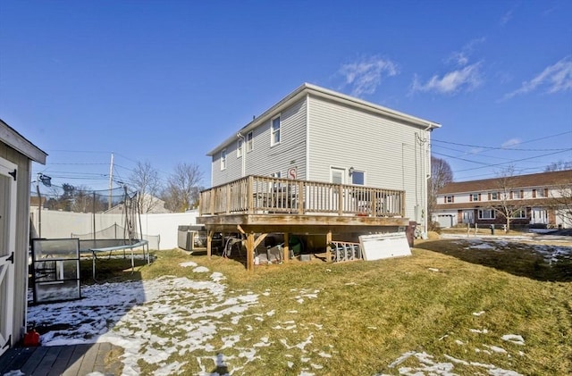 snow covered property featuring a wooden deck, a yard, and a trampoline