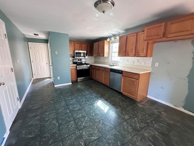 kitchen with baseboards, light countertops, appliances with stainless steel finishes, brown cabinets, and backsplash