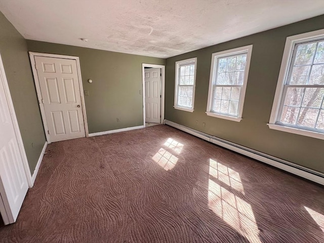 carpeted spare room with a baseboard heating unit, baseboards, a textured ceiling, and a healthy amount of sunlight