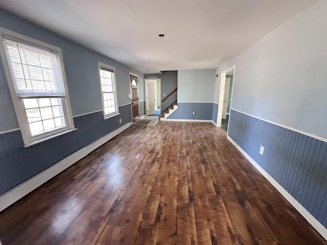 unfurnished room featuring stairs, wood finished floors, a wainscoted wall, and baseboards