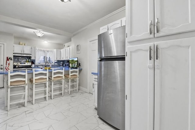 kitchen featuring white cabinetry, appliances with stainless steel finishes, crown molding, and a kitchen bar