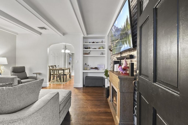 living room with dark wood-type flooring, an inviting chandelier, beam ceiling, and built in shelves