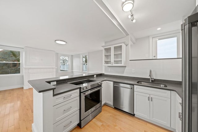 kitchen featuring sink, tasteful backsplash, kitchen peninsula, white cabinets, and appliances with stainless steel finishes