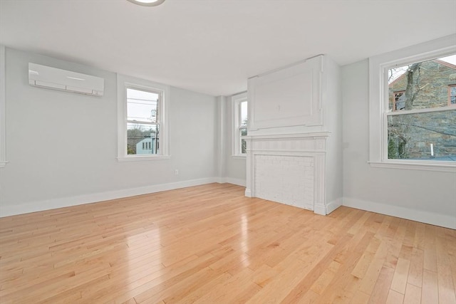 empty room with a wall mounted air conditioner, light wood-type flooring, and a healthy amount of sunlight