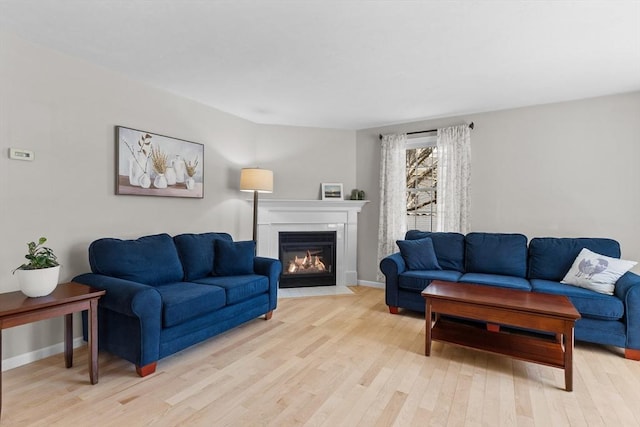 living room featuring light wood-style floors, baseboards, and a fireplace with flush hearth