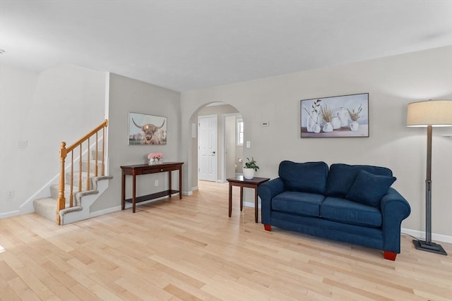 living room with stairway, arched walkways, baseboards, and light wood finished floors