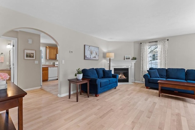 living area with light wood-style floors, arched walkways, a fireplace with flush hearth, and baseboards