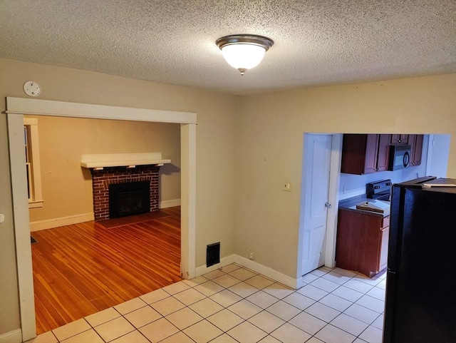 kitchen featuring light tile patterned floors, a textured ceiling, a brick fireplace, and black appliances