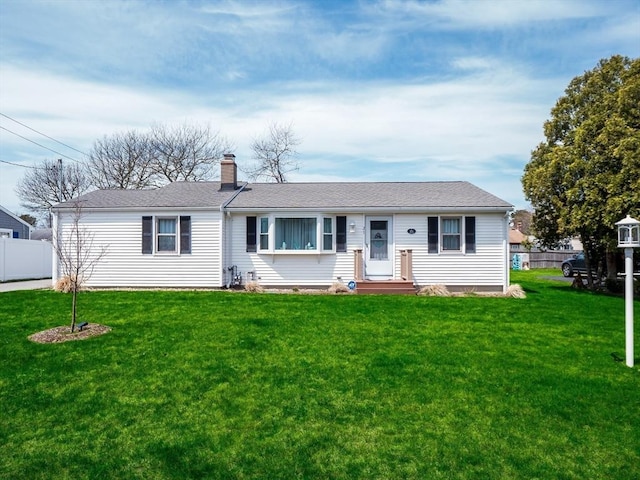 ranch-style house with a front yard, fence, roof with shingles, and a chimney