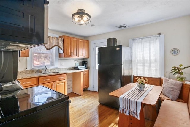 kitchen featuring a sink, light wood-type flooring, black appliances, and visible vents