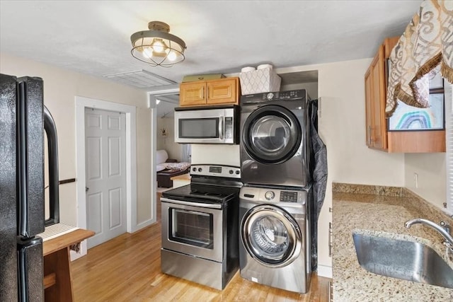 laundry room with visible vents, laundry area, light wood-style flooring, a sink, and stacked washer and dryer