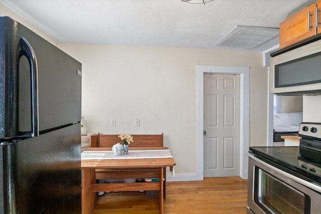 kitchen featuring light wood finished floors, stainless steel electric stove, baseboards, and freestanding refrigerator