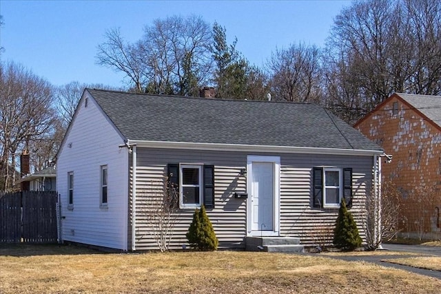 view of front facade with entry steps, fence, a front lawn, and roof with shingles