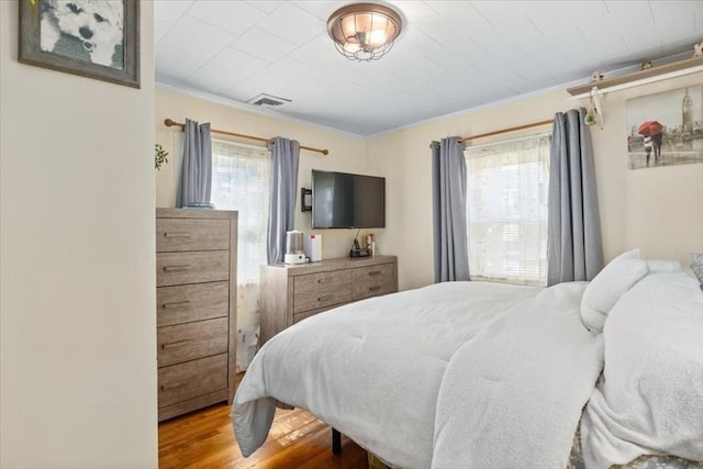 bedroom with visible vents, crown molding, and wood finished floors