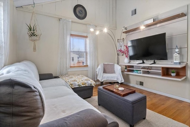 living room with vaulted ceiling, visible vents, baseboards, and wood finished floors