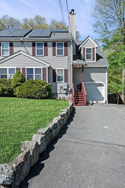 view of property with a front lawn, roof with shingles, a chimney, driveway, and solar panels