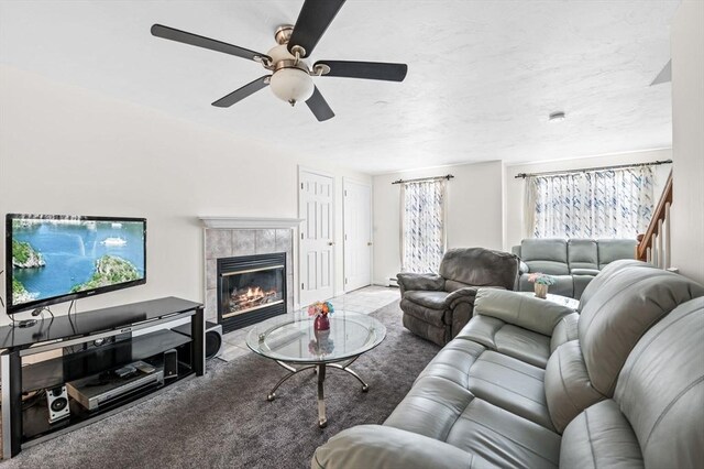 carpeted living area with a tiled fireplace and a ceiling fan