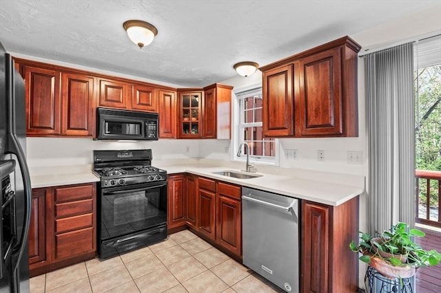 kitchen featuring a sink, light tile patterned floors, light countertops, black appliances, and glass insert cabinets
