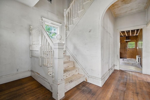 staircase featuring hardwood / wood-style flooring, arched walkways, plenty of natural light, and radiator