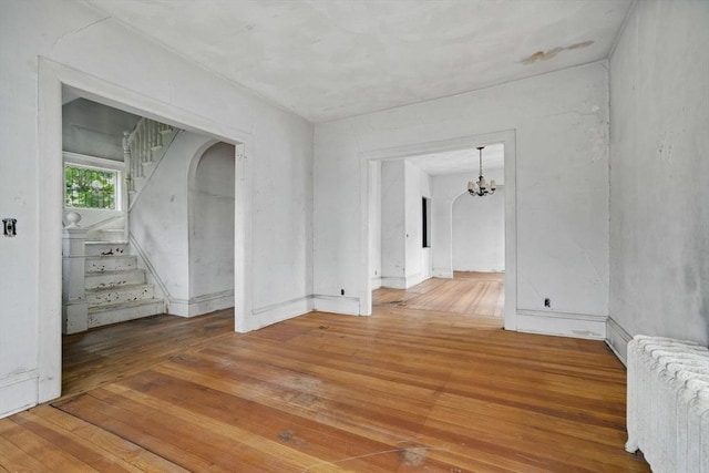 empty room featuring radiator, hardwood / wood-style flooring, a chandelier, and stairway