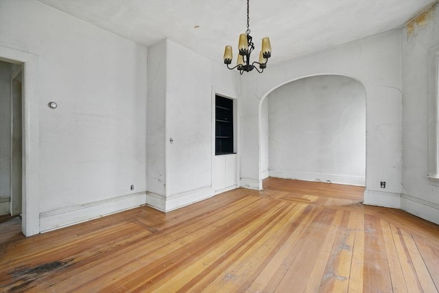 unfurnished dining area featuring arched walkways, light wood-style floors, and a chandelier