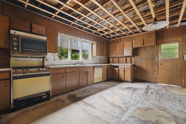 kitchen with white dishwasher, wall oven, light countertops, wooden walls, and a sink