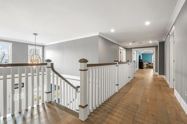 hall featuring wood-type flooring, a notable chandelier, and ornamental molding