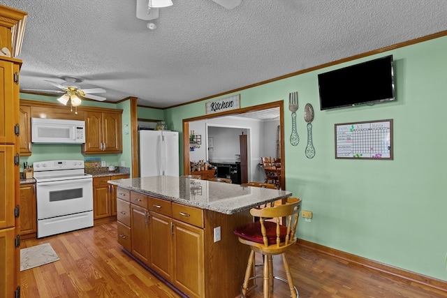 kitchen featuring a center island, a kitchen breakfast bar, light hardwood / wood-style flooring, white appliances, and ornamental molding