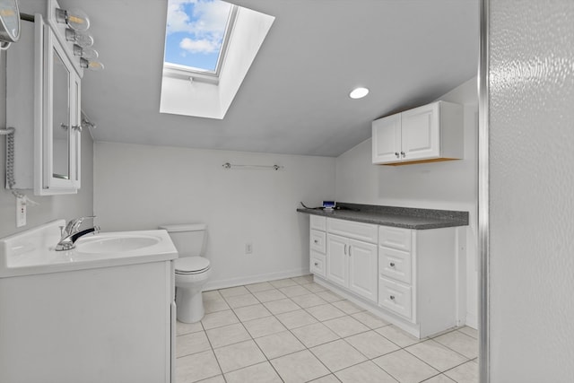 bathroom featuring lofted ceiling with skylight, tile patterned flooring, vanity, and toilet