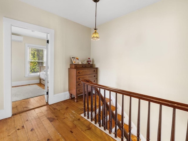 corridor featuring baseboards, a wall unit AC, light wood finished floors, and an upstairs landing