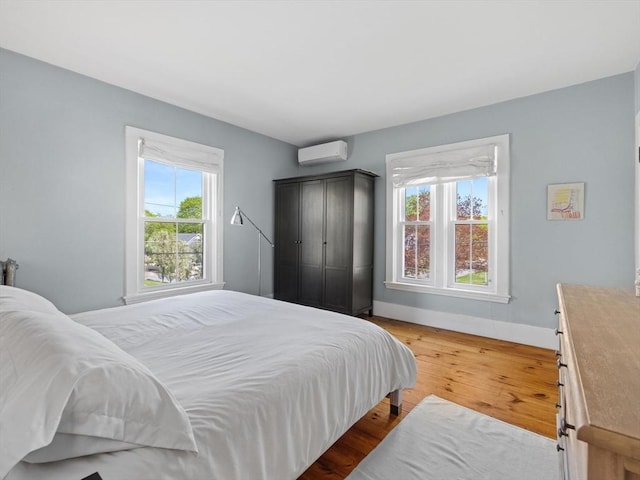 bedroom featuring baseboards, a wall mounted AC, and wood finished floors