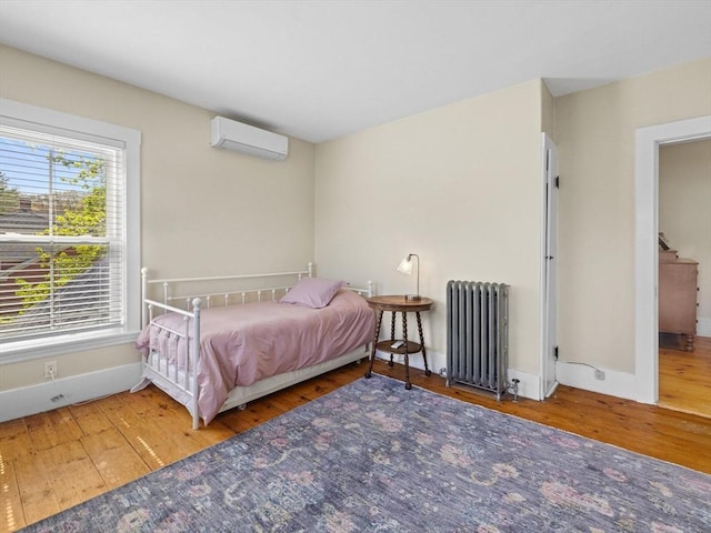 bedroom featuring baseboards, a wall mounted AC, radiator heating unit, and hardwood / wood-style floors