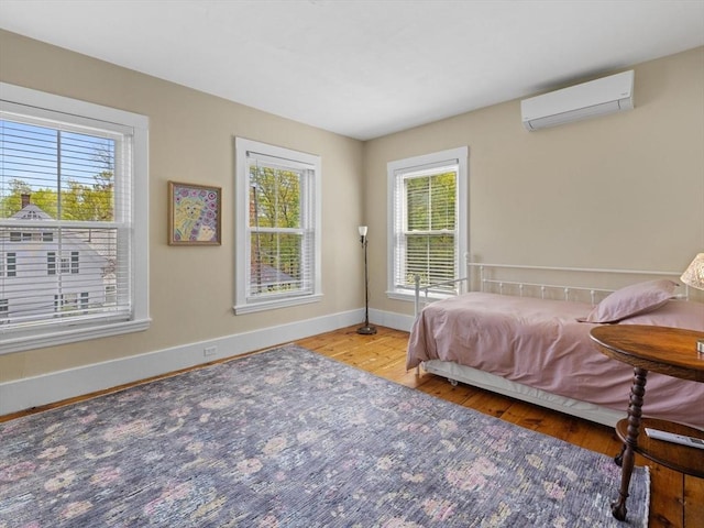 bedroom featuring multiple windows, wood finished floors, and a wall mounted air conditioner